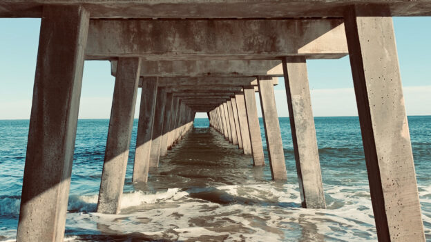 Photograph of the sea and the underneath of a wooden pier from the beach